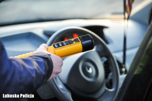 Policjant trzymający alkomat, a w tle wnętrze pojazdu.