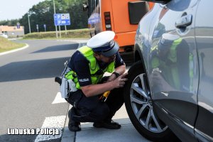 Policjant sprawdza stan ogumienia w oponach.