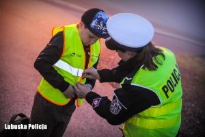 Policjantka zakłada dziecku kamizelkę odblaskową.