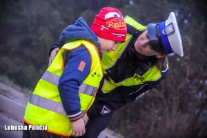 Policjantka zakłada dziecku kamizelkę odblaskową.