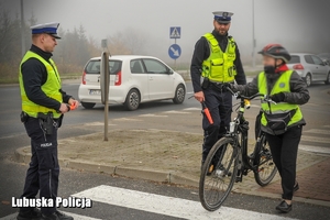 policjanci pomagają przejść rowerzystce przez przejście
