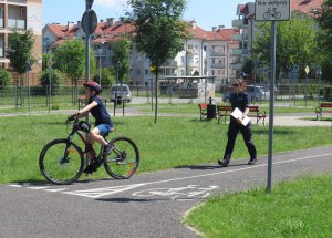 Dziecko podczas egzaminów na kartę rowerową na miasteczku ruchu drogowego pod czujnym okiem policjantki..