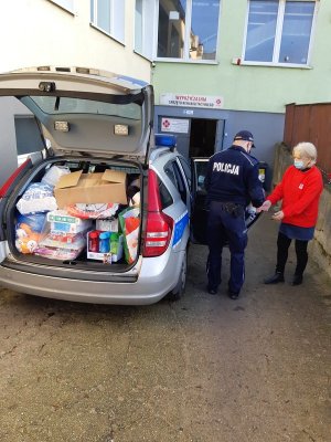 policjant przekazuje paczki pracownicy Caritasu