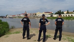 Policjantka kontroluje ze strażnikami miejskimi miejsce objęte zakazem kąpieli.