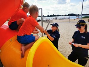 Na zdjęciu dzieci będące na plaży otrzymują odblaski od policjantki