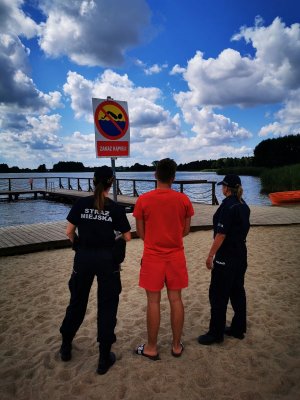 Na zdjęciu widać jak na plaży stoi ratownik ,policjantka oraz strażniczka miejska