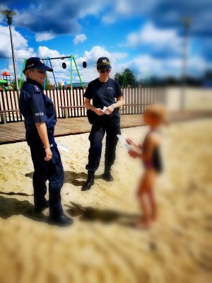 Na zdjęciu policjantka rozmawia z dzieckiem o bezpiecznym plażowaniu