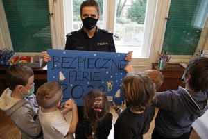 Policjantka pokazuje dzieciom plakat Bezpieczne Ferie