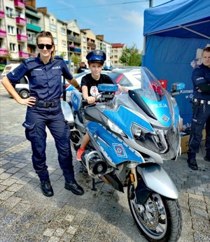Na zdjęciu motocykl policyjny na którym stoi dziecko i obok policjantka