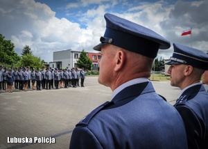 Policjanci stojący w szeregu, a w tle flaga Polski.