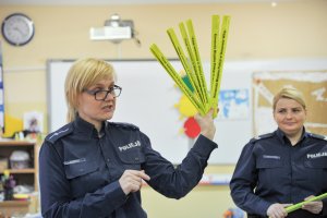 Dwie policjantki, jedna trzyma opaski odblaskowe.